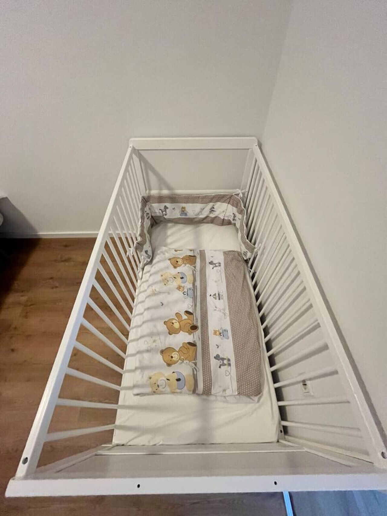 Ein weißes Babybett mit einer beigen Matratze und einer Decke mit Bärenmotiv.