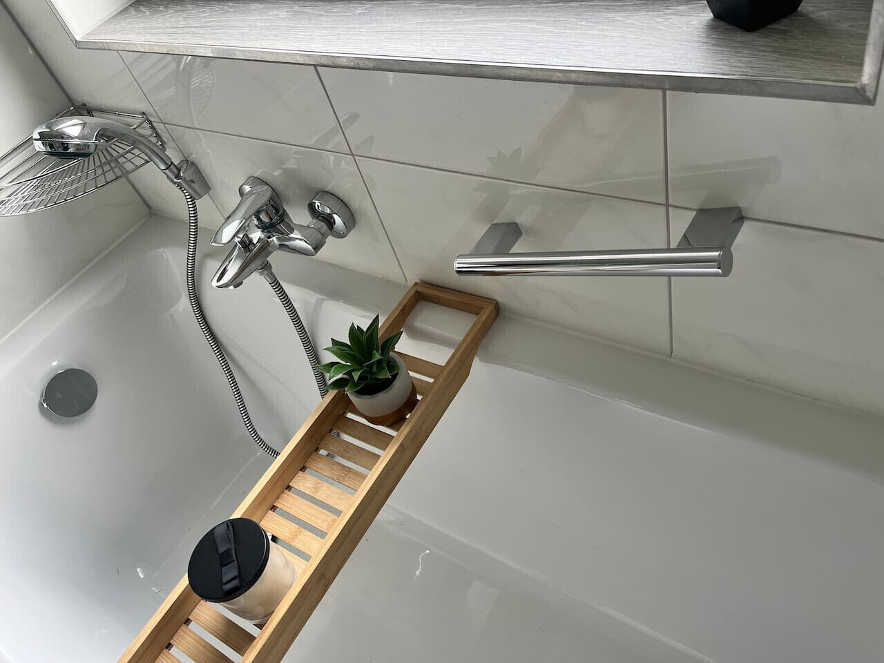 A modern bathroom with a bathtub, a shower, and a wooden shelf with a potted plant.