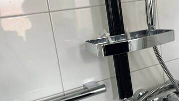A modern bathroom with a chrome showerhead, a handheld shower, and a chrome towel bar.