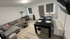 Ett modernt vardagsrum med en grå soffa, ett svart soffbord med cirkelformade utskärningar, en vit bänk och en platt-TV som är monterad på väggen.