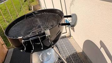Een barbecue met een metalen rooster, deksel en handvat op een balkon.