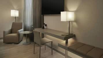 A modern hotel room with a sofa, a chair, a small round table, a desk, and two lamps.