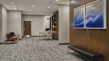 A modern hotel lobby with a carpeted floor, a wooden bench, a desk with a chair, and a bookshelf.