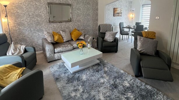 A modern living room with a grey patterned wall, a white coffee table, and grey sofas with yellow cushions. - Ayr Refurbished May 2024 3 Bedroom 140m2 Detached House With Private Gardens (Ayr)