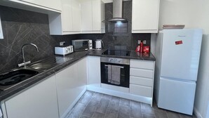 A compact kitchen with white cabinets, a black countertop, a built-in oven, a microwave, a gas stove, a sink, and a white refrigerator. - Ayr Refurbished May 2024 3 Bedroom 140m2 Detached House With Private Gardens (Ayr)