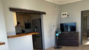 A modern kitchen with a refrigerator, oven, and microwave. There is a wooden countertop and cabinets. A fan is on the floor next to a TV on a dresser. - Wake up to gorgeous sunrises and sea views upon a wooden balcony. (Amanzimtoti)