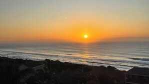 A sunset over the ocean with buildings in the foreground. - Wake up to gorgeous sunrises and sea views upon a wooden balcony. (Amanzimtoti)