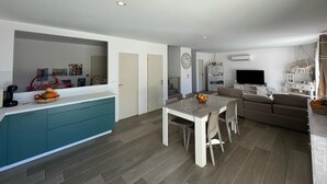 A modern kitchen with teal cabinets, a dining area with a white table and chairs, a living room with a sofa, and a TV. - Superb house with garden and swimming pool close to transport links  (Avignon)