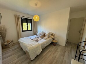 Ein Schlafzimmer mit einem Bett, einem Fenster mit Vorhängen, einer Hängelampe und einer Tür.