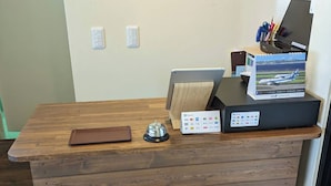Un mostrador de recepción de madera con una caja registradora, una pequeña bandeja y una caja de folletos.