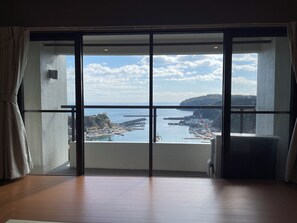 Habitación con un amplio ventanal corredera que da a un balcón con vistas a la costa, incluyendo barcos y un muelle.