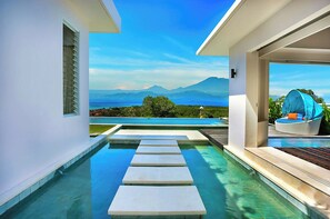 A modern pool area with a clear view of mountains and a body of water in the background.