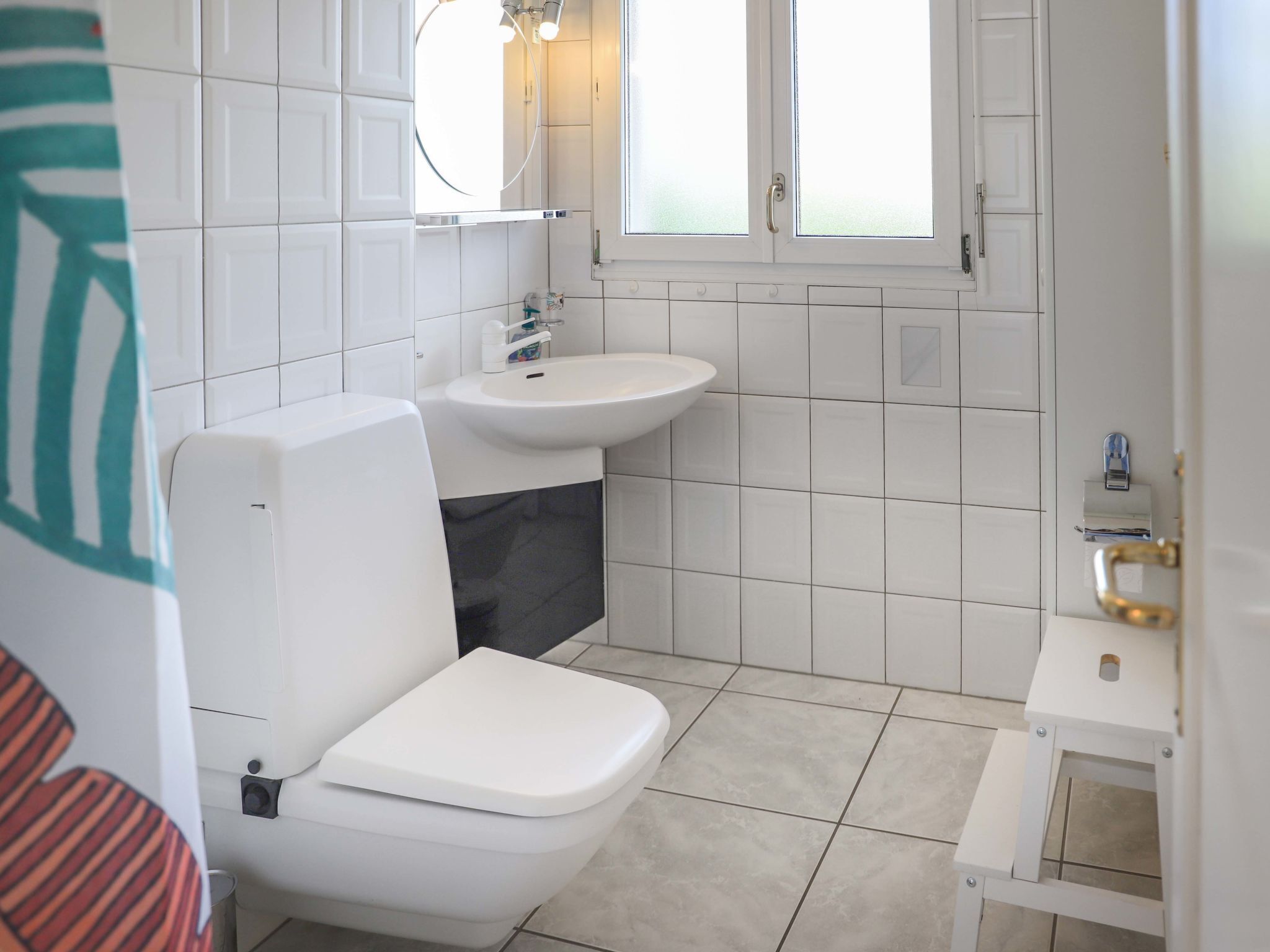 A small, clean bathroom with white fixtures, a toilet, a sink, and a window.