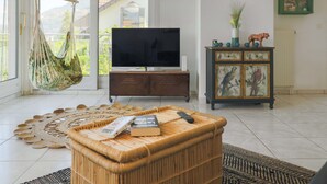 Una sala de estar con televisor, una silla colgante, un mueble con cuadros enmarcados y un ventanal grande.