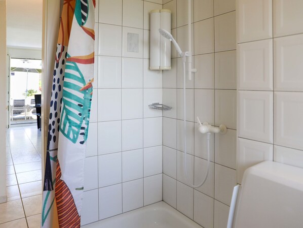 A bathroom with white tiled walls, a shower with a handheld showerhead, and a toilet.