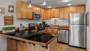 A modern kitchen with wooden cabinets, stainless steel appliances, a black countertop island, and pendant lighting.