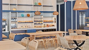 Un café avec des tables en bois et des chaises en osier, des étagères remplies de pâtisseries et des lampes en osier suspendues au plafond.