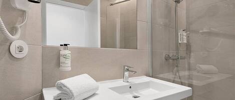 Un baño moderno con un lavabo blanco, un espejo y una cabina de ducha de vidrio.