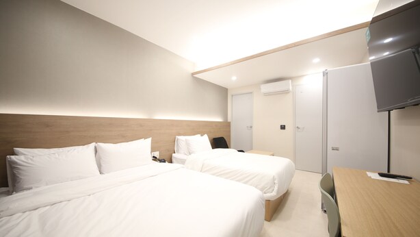 Una habitación de hotel con dos camas, un escritorio, una silla, un televisor y una puerta.
