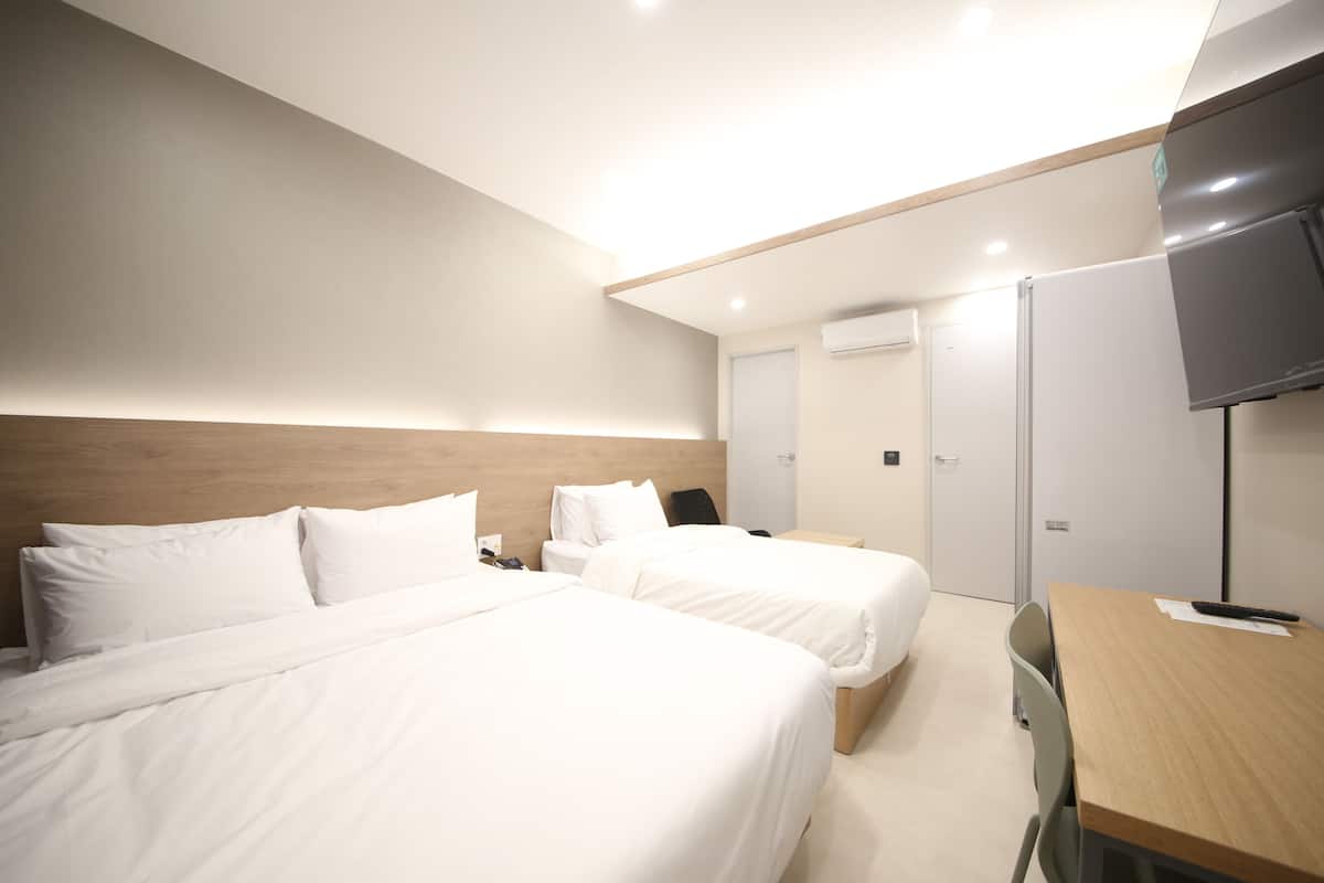 A hotel room with two beds, a desk, a chair, a TV, and a door.