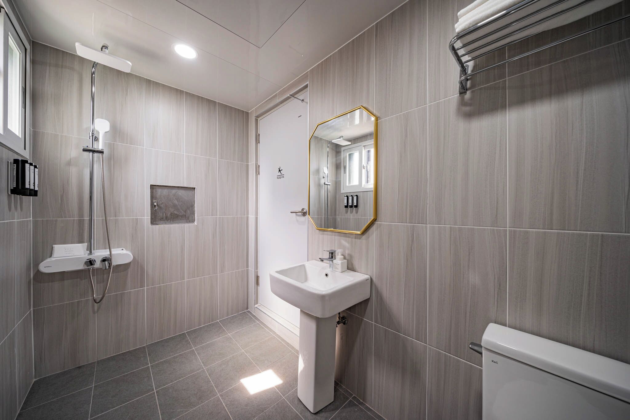 Un baño moderno con ducha, lavamanos, inodoro y espejo con marco dorado.