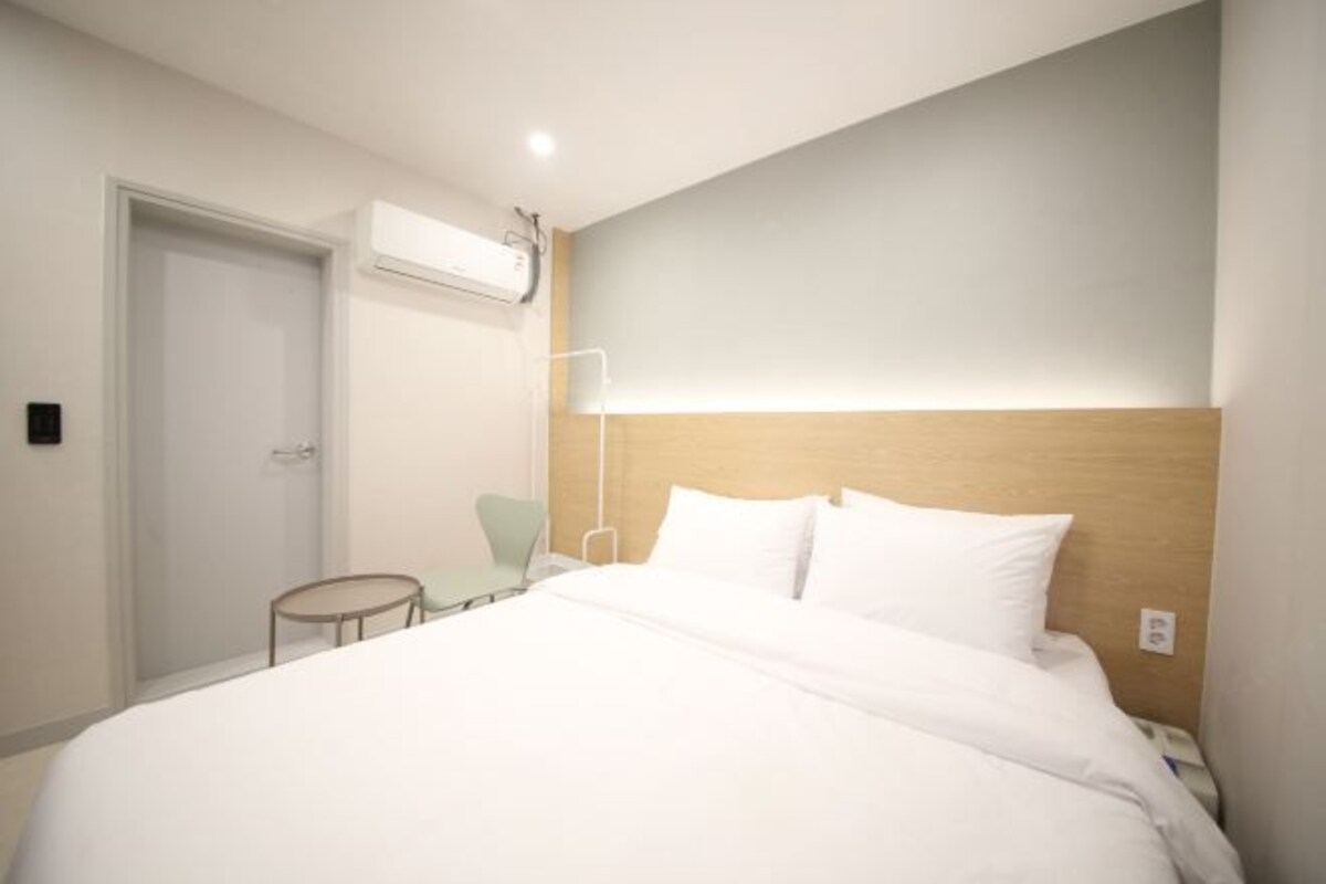 Ein modernes Hotelzimmer mit einem großen Bett, einem Nachttisch, einem Sessel und einer Klimaanlage.