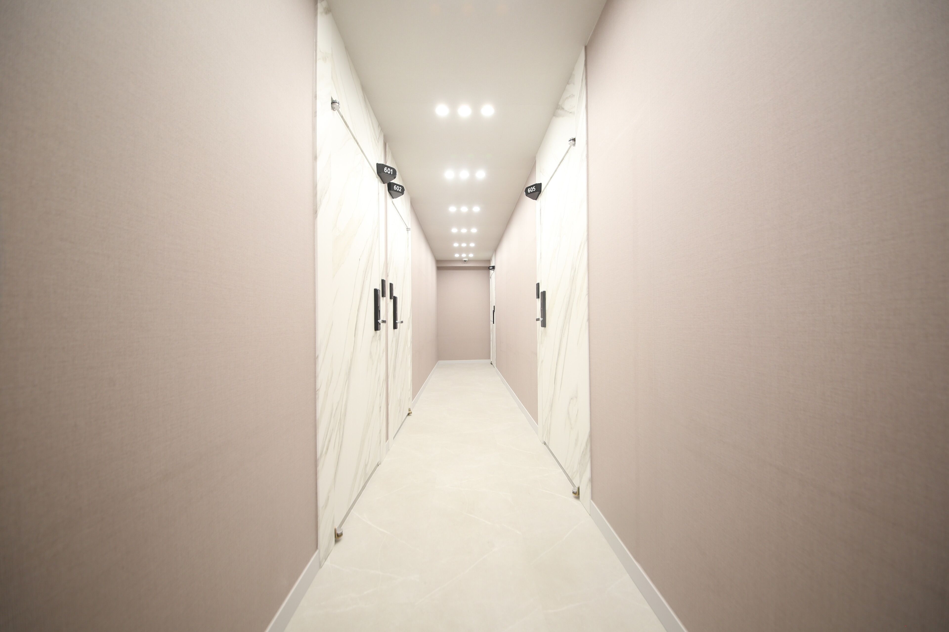 A corridor with lockers and a tiled floor, leading to a door at the end.