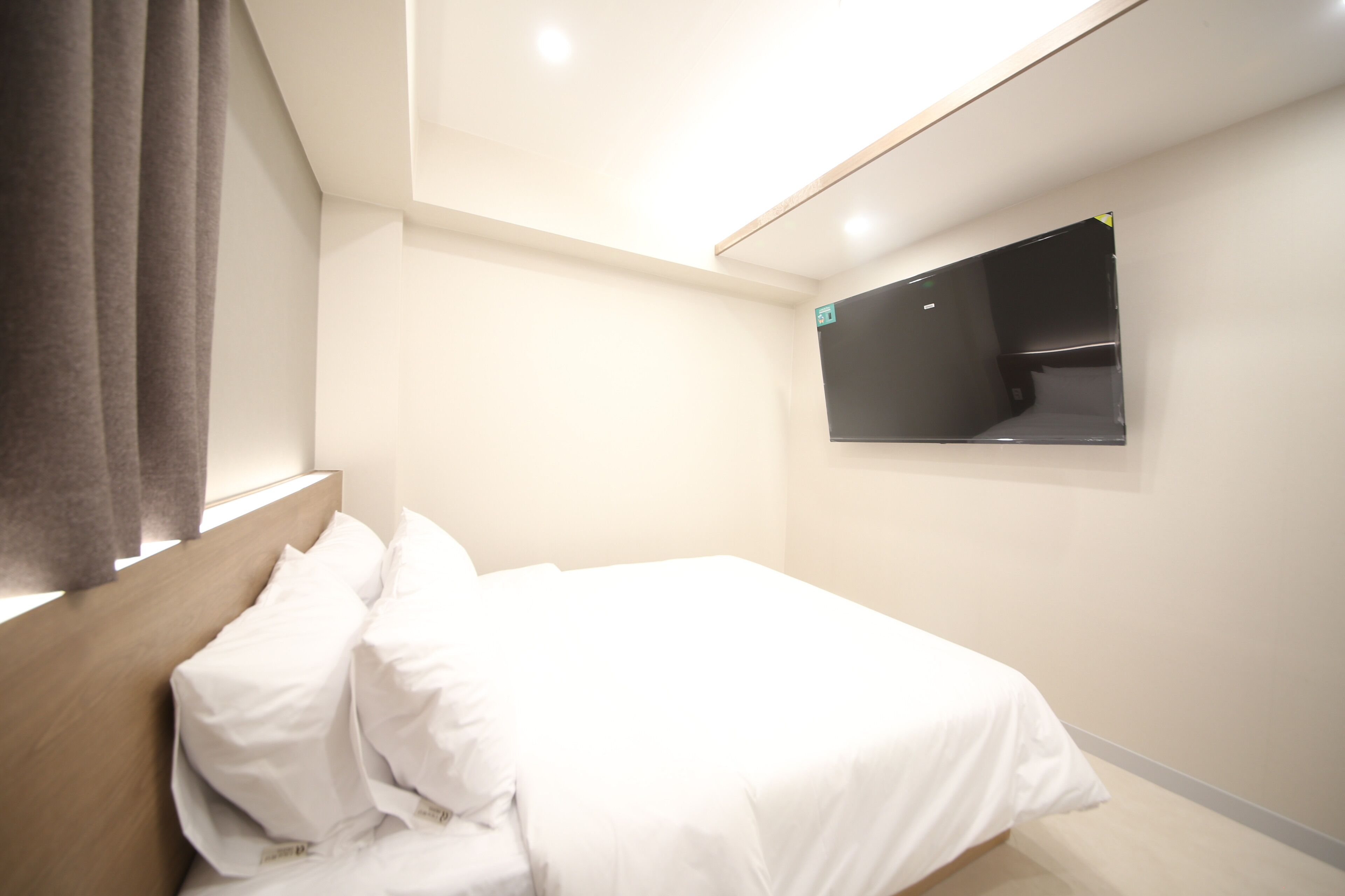 A hotel room with a bed, a mounted TV, and a window with curtains.