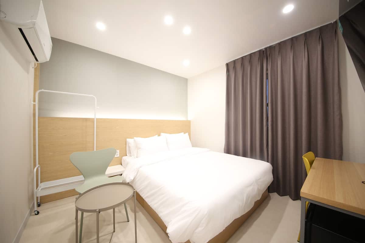 A hotel room with a bed, a small round table, a chair, a heater, and a window with curtains.
