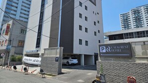 Un moderno edificio de hotel con un cartel llamativo que dice "Calm Rest Hotel" y un letrero que indica la existencia de un estacionamiento.
