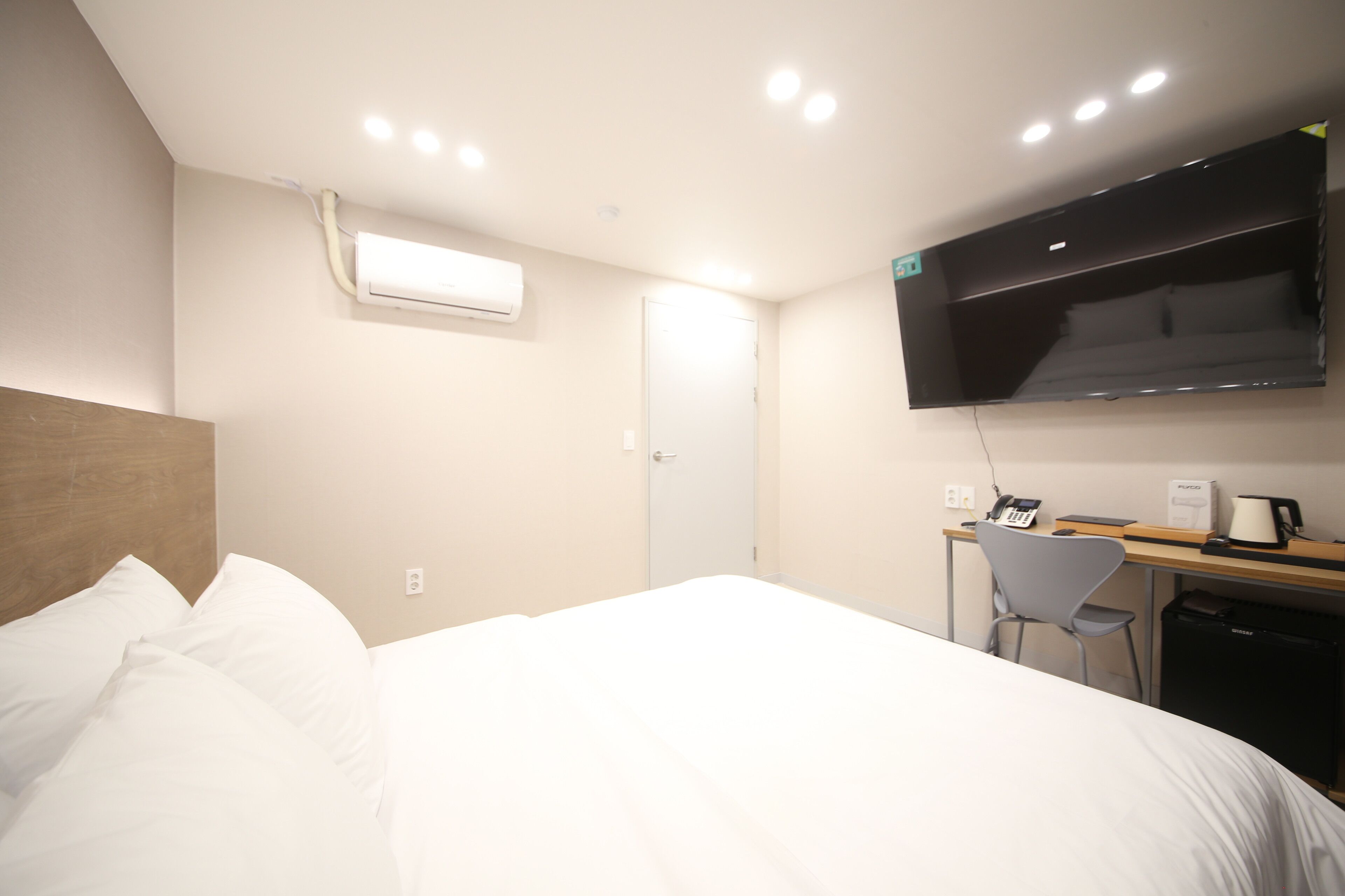 A hotel room with a bed, a desk, a chair, a TV, and an air conditioning unit.