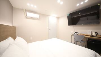 A hotel room with a bed, a desk, a chair, a TV, and an air conditioning unit.