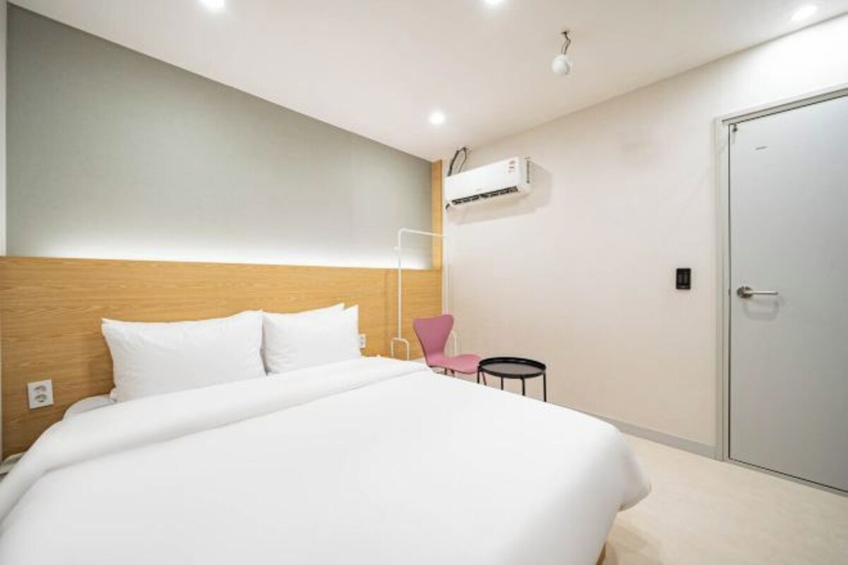 A hotel room with a bed, a chair, a small table, and a wardrobe.