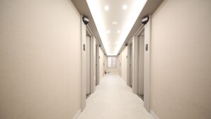 Un pasillo largo y estrecho con puertas a ambos lados, letreros con números sobre cada puerta y suelo de baldosas.