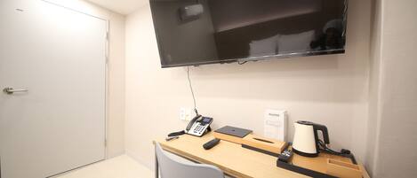 A hotel room with a desk, chair, flat-screen TV, telephone, and a coffee maker.