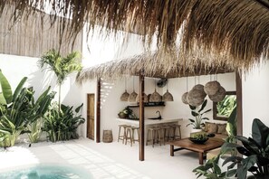 A tropical-style interior with a thatched roof, a pool, and lush greenery. - Villa Almaz (Seminyak)