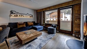 Een moderne woonkamer met een donkerblauwe bank, een houten salontafel en een groot raam met uitzicht op gebouwen.