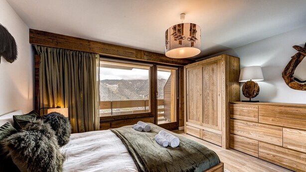 Een slaapkamer met een groot bed, een houten garderobe en uitzicht op de omgeving.