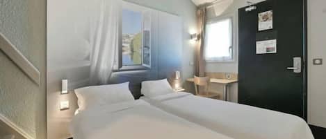 A hotel room with two beds, a desk, a chair, a window with curtains, and a door with a bulletin board.