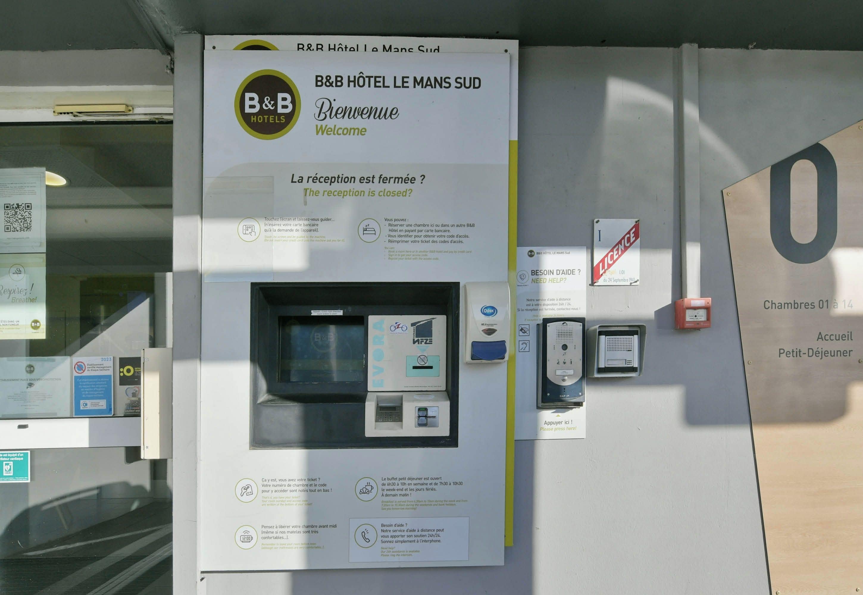 A B&B hotel reception area with a closed reception sign, a self-service kiosk, and a room number sign.