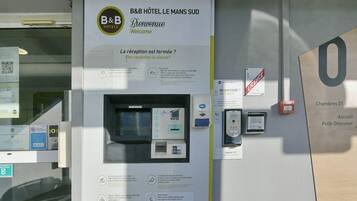Ein Empfangsbereich eines Bed and Breakfast mit geschlossenem Empfangsschild, einem Selbstbedienungs-Check-in-Terminal und einem Schild mit Zimmernummern.
