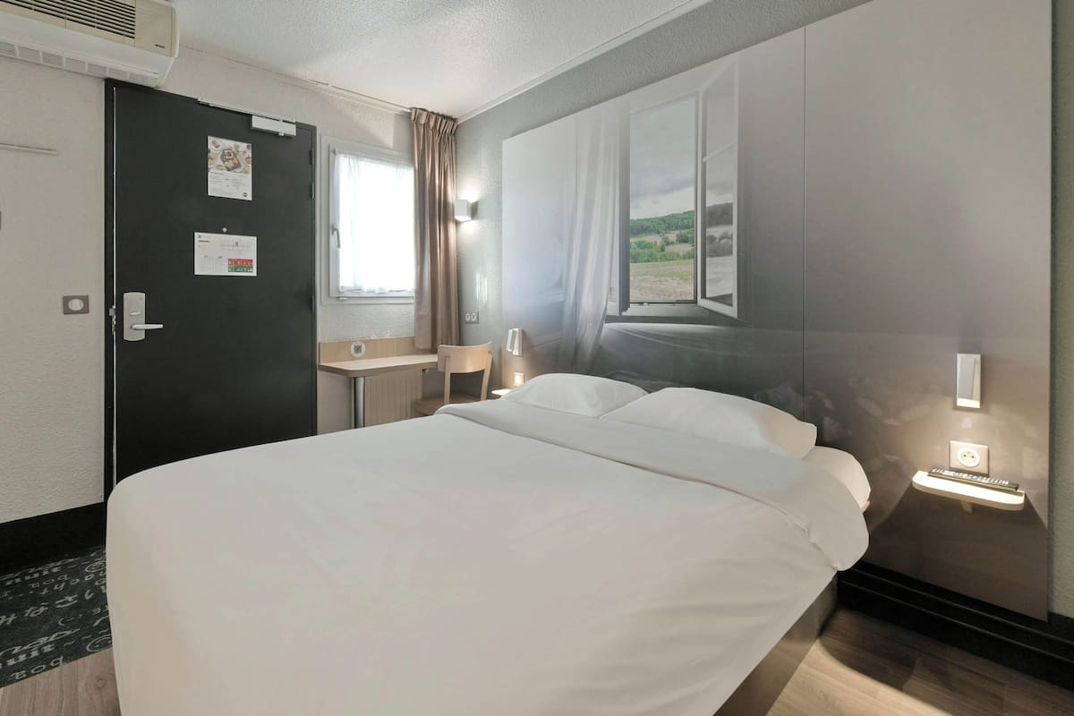 Een hotelkamer met een bed, een bureau, een stoel, een raam met gordijnen en een wandlamp.
