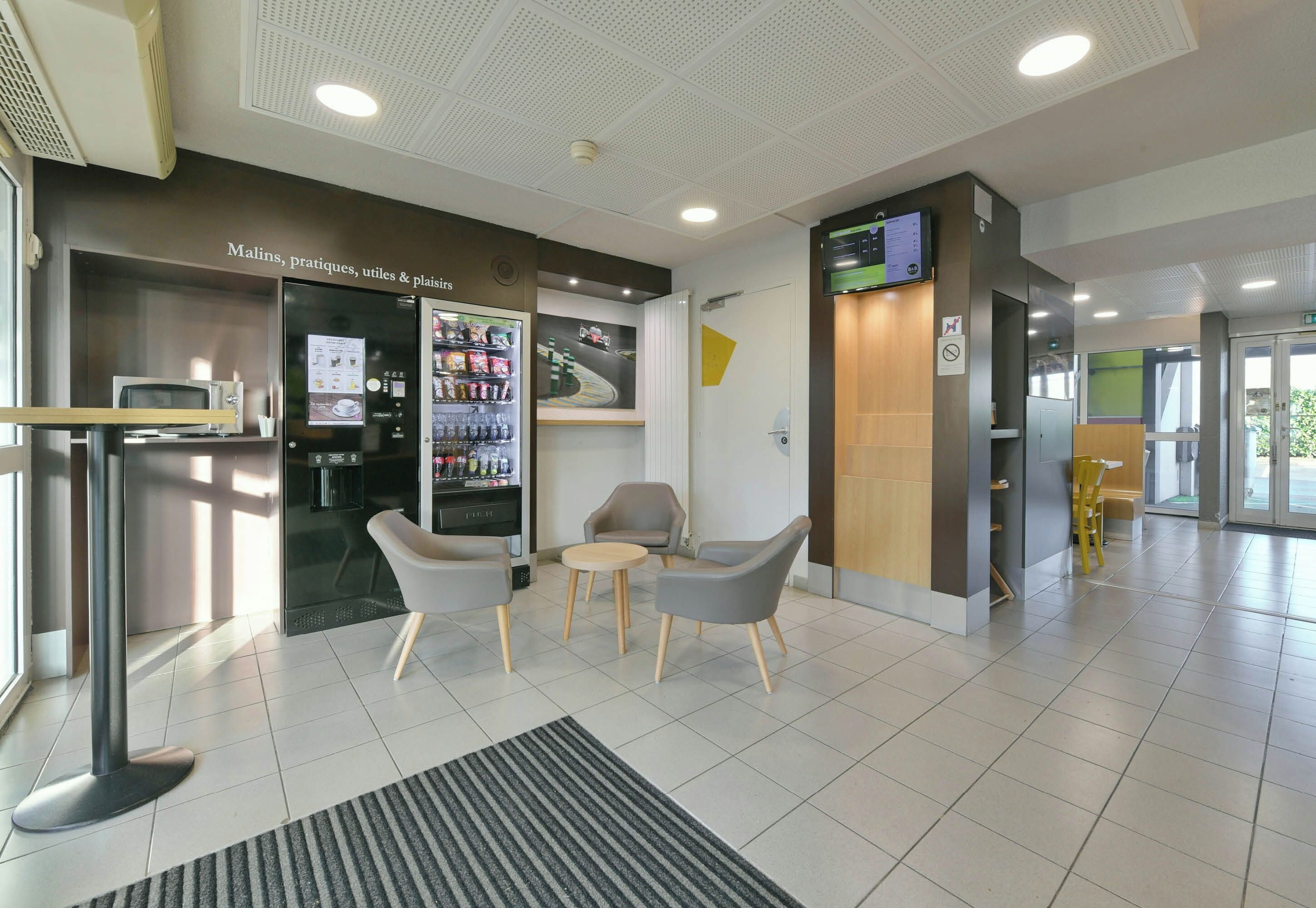 A modern lobby with seating, a vending machine, and a digital display.