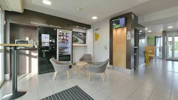A modern lobby with seating, a vending machine, and a digital display.