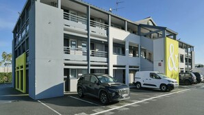 A multi-story building with a parking area, a white van, and a black car parked in front.