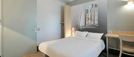 A hotel room with a bed, a desk, a chair, a painting on the wall, and a door.