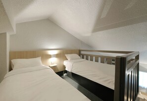 A room with two beds, a nightstand, a wall-mounted lamp, and a sloped ceiling. - B&B Hotel Le Mans Sud (Arnage)