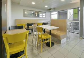 A restaurant interior with yellow and white chairs, a wooden bench, and a tiled floor. - B&B Hotel Le Mans Sud (Arnage)
