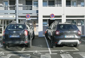 Deux voitures Duster sont garées sur un parking, avec un bâtiment portant l’inscription « ACCUEIL » en arrière-plan.