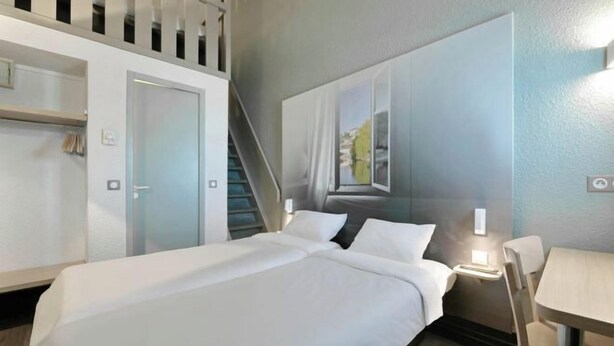 Ein Hotelzimmer mit Bett, Schreibtisch und Stuhl. Ein Fenster bietet Blick auf Grünflächen.